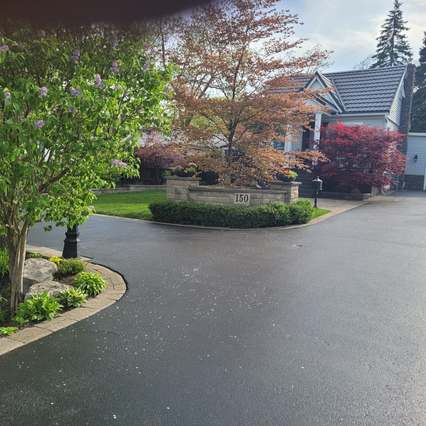 Circular asphalt driveway sealed around a stone planter with stamped concrete edging