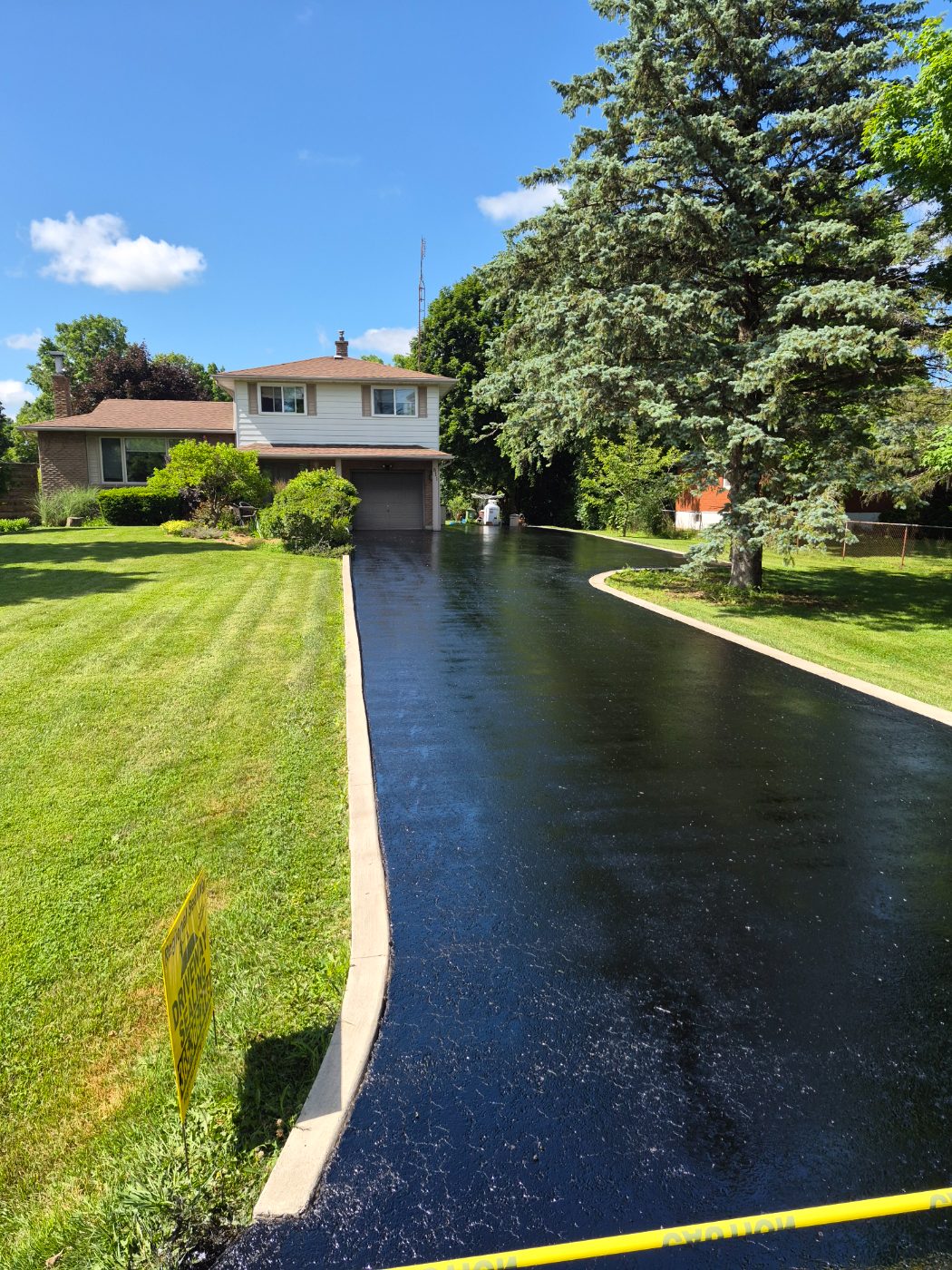 Long country driveway sealed deep black, taped off with a Regional Sealing lawn sign in place
